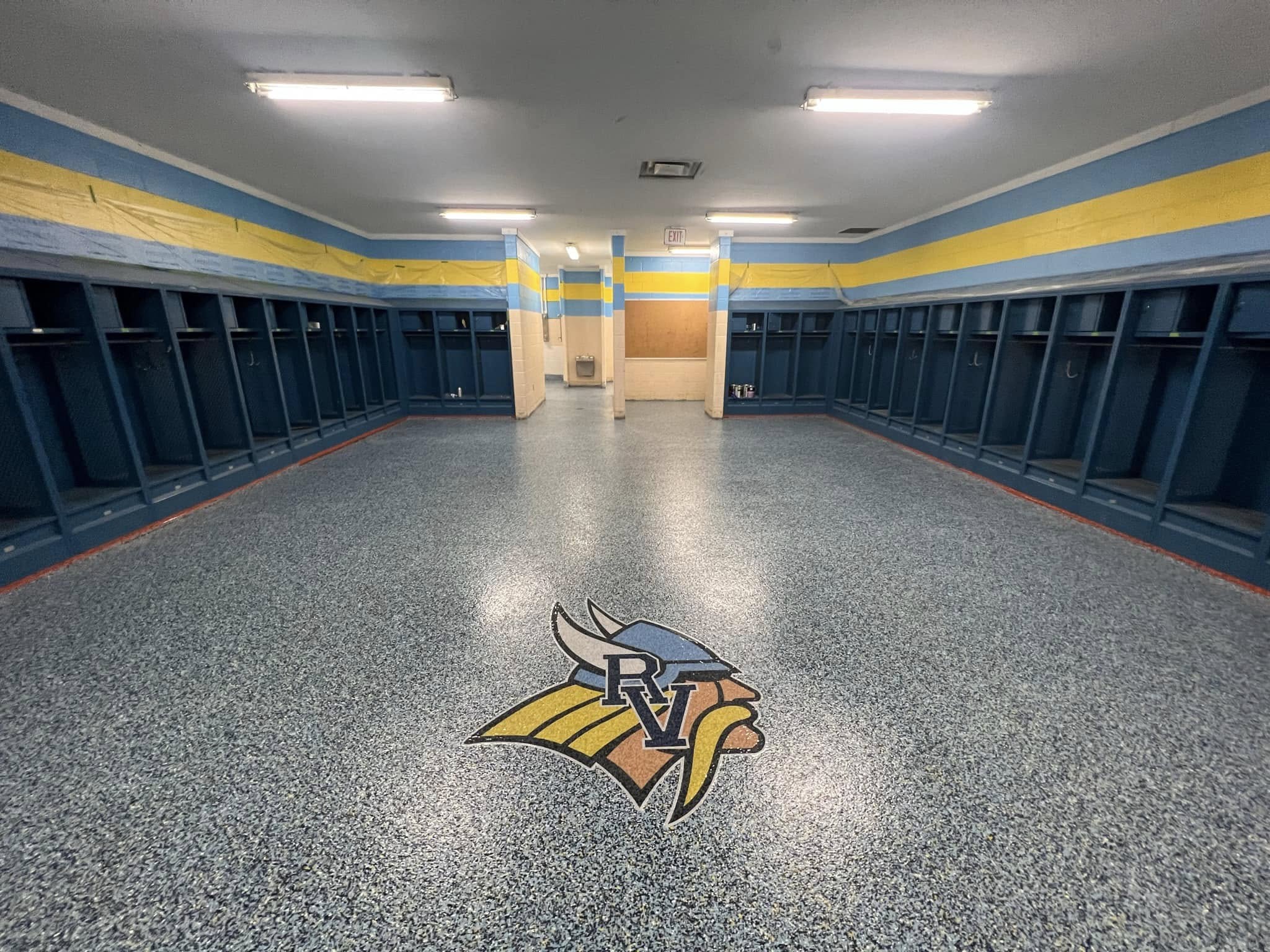 Blue and gray flake epoxy floor in a school locker room with the River Valley Vikings logo medallion