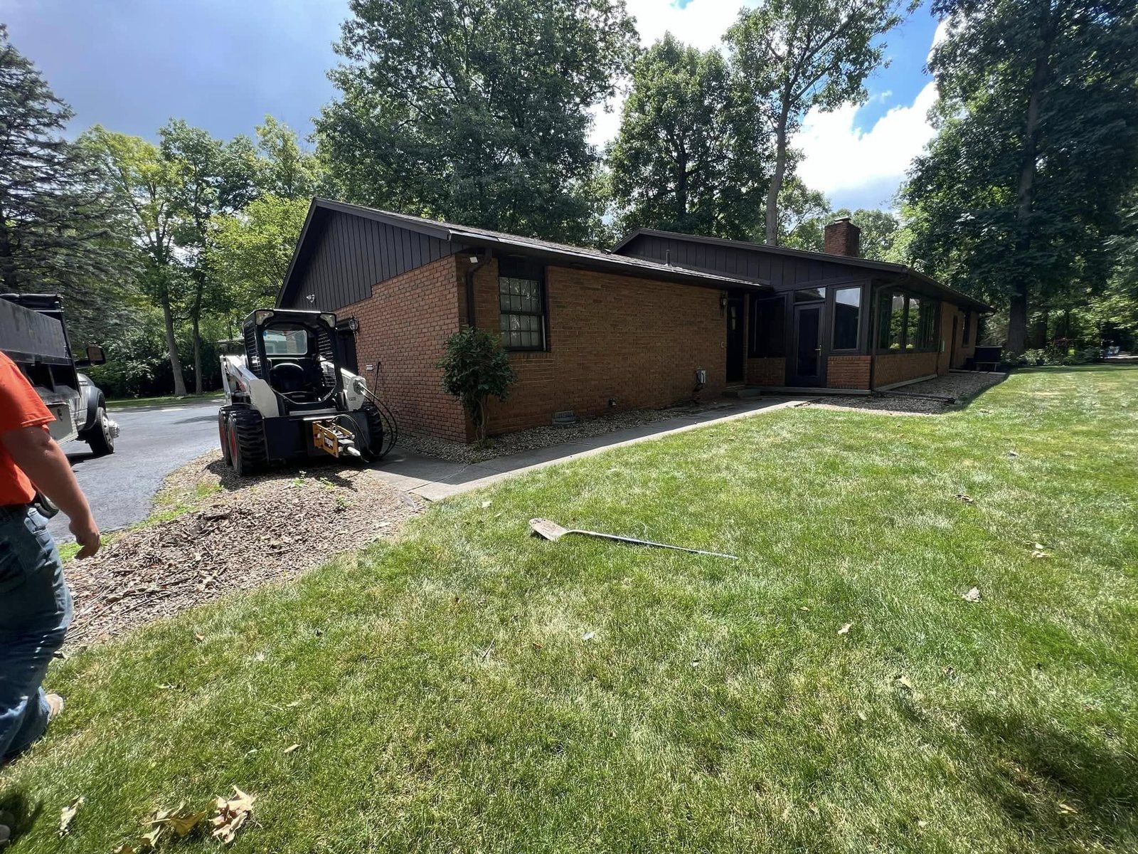 Brick ranch home with a bare dirt entrance and a Bobcat before the new driveway was poured