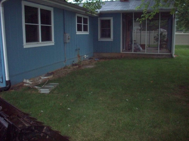 Grass backyard beside a blue house and screened porch before the patio was poured
