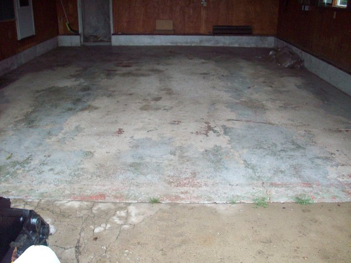Cracked and stained garage floor in a wood-paneled garage before demolition